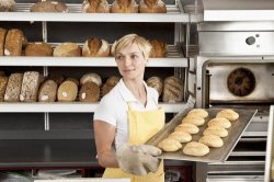 Девушка в цеху пекарни держит на подносе свежеиспечённый хлеб